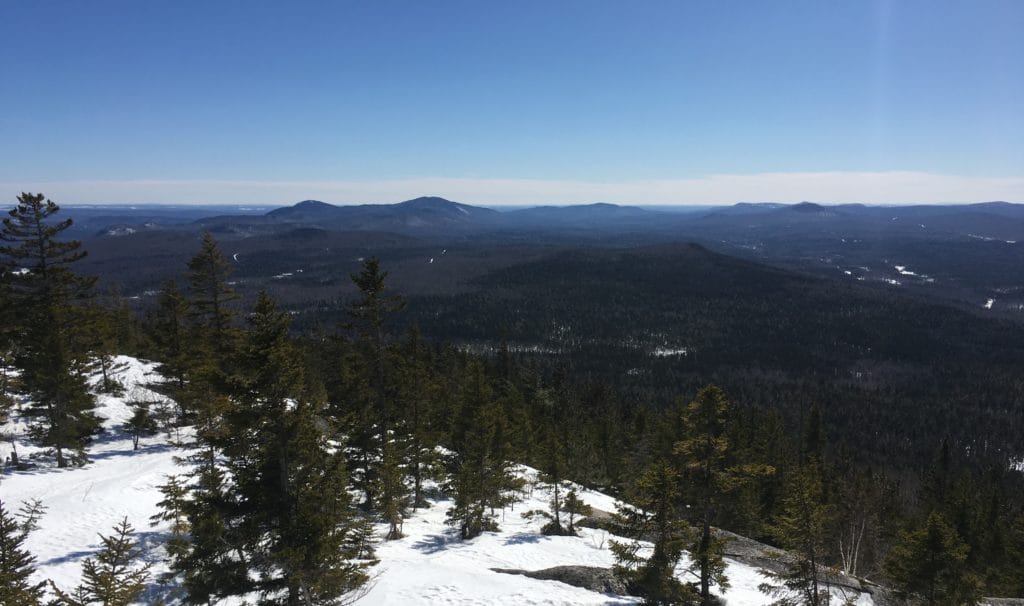 A view showcases snowy forests and distant mountains in the Katahdin Woods