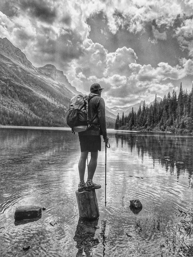 Hiker Grizzly standing on a log in a lake.