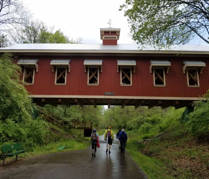 Three hikers crossing under a covered bridge along the Buckeye Trail.