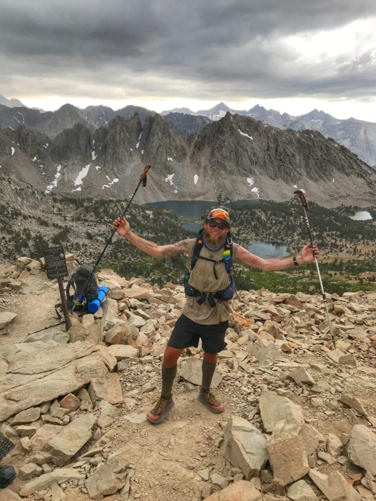 Thru-Hiker Crunchmaster posing on the PCT, the Sierra Nevada mountain range behind him.