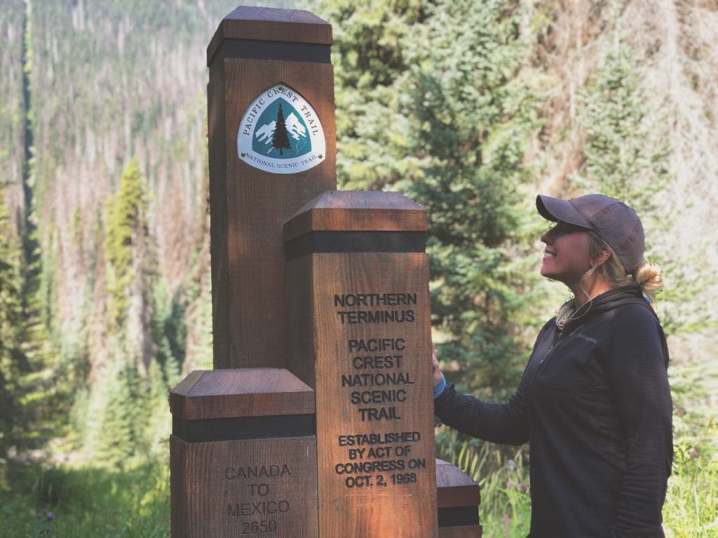 A PCT thru-hiker standing next to the northern terminus.