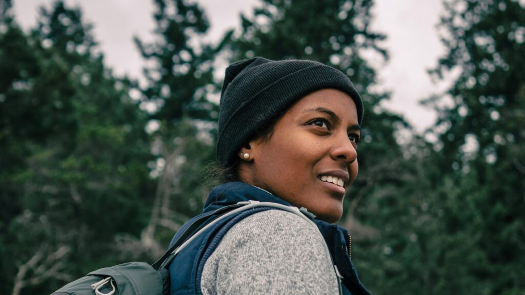A woman wearing a black beanie and grey shirt out in the forest