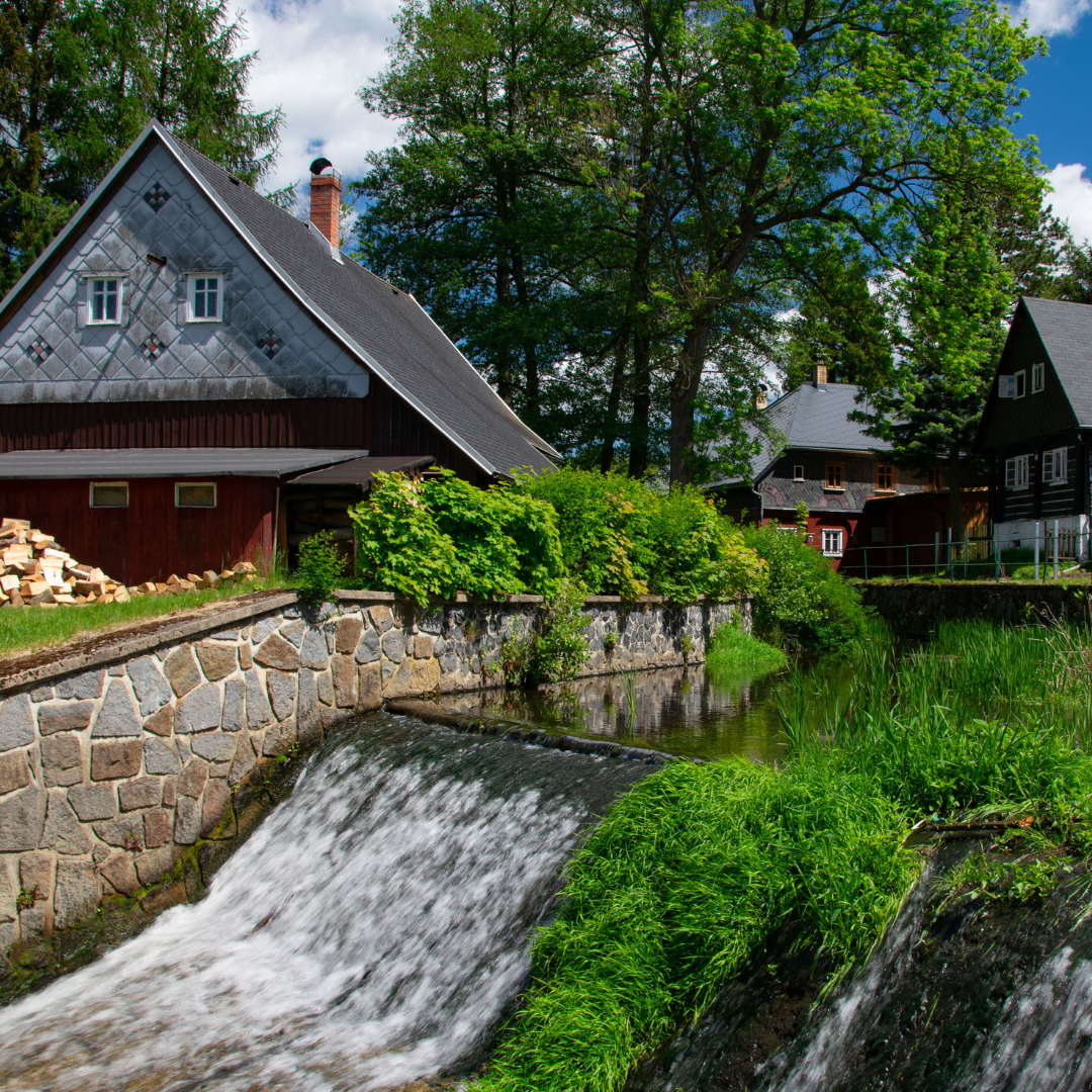 A flowing river snd small water fall with homes surrounding the area in thje Czech