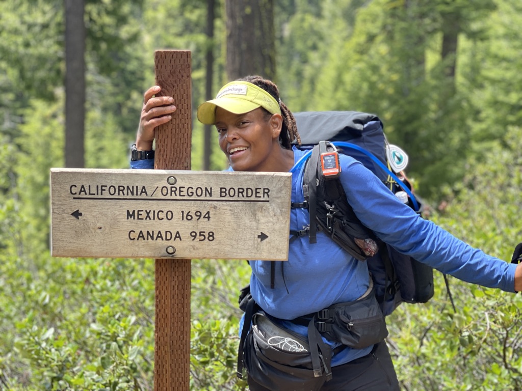A hiker smiling next to a Pacific Crest Trail sign