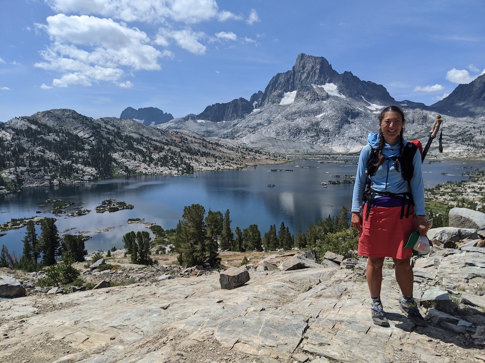 A woman hiking the Pacific Crest Trail standing with a lake and mountain in the background