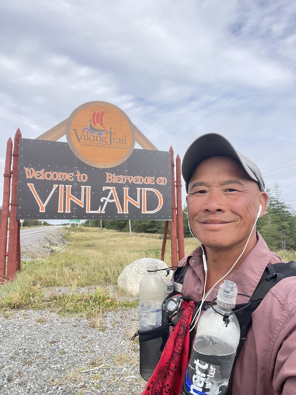 A hiker smiling next to a sign for the Viking Trail in Newfoundland