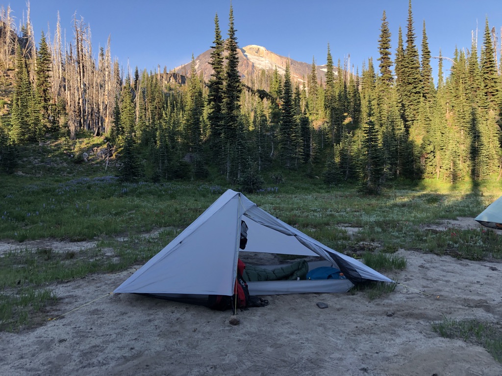 a tent set up with trees and a mountain in the background