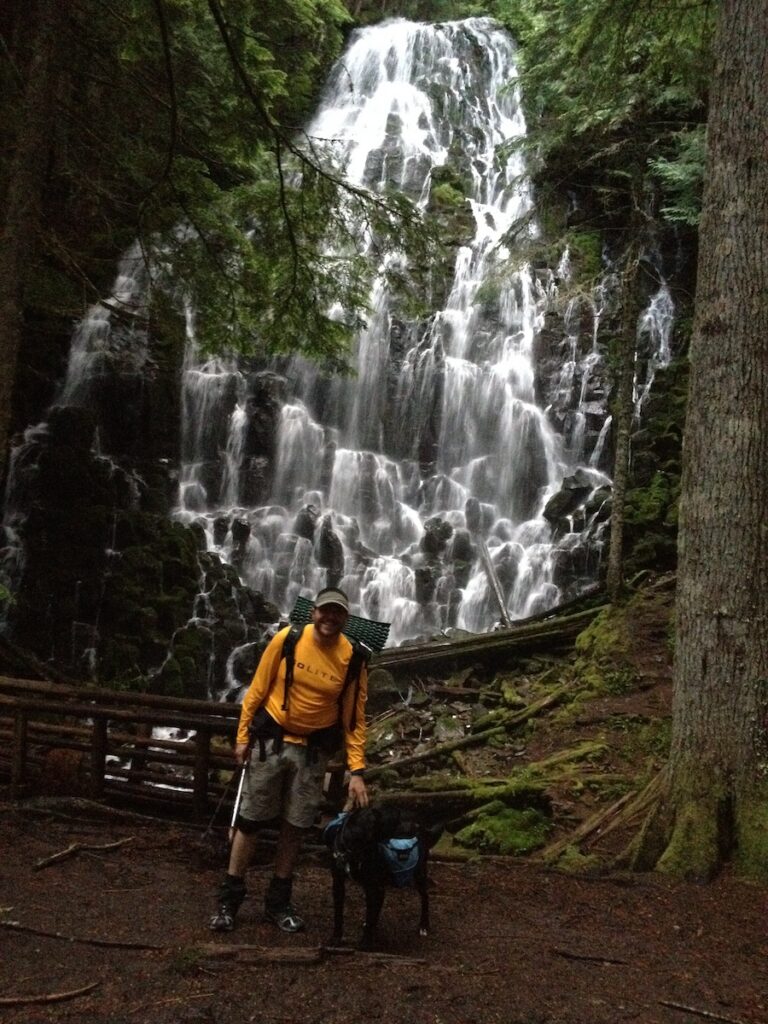 a hiker and his dog standing in front of Ramona Falls