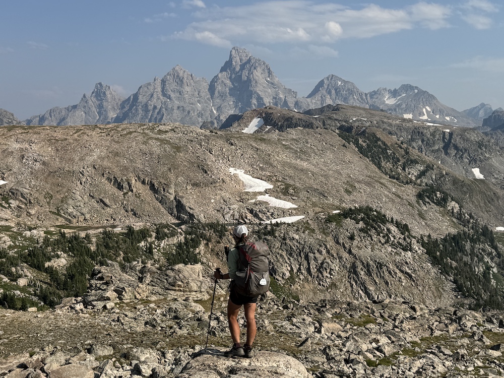 a hiker standing with the Tetons in the background