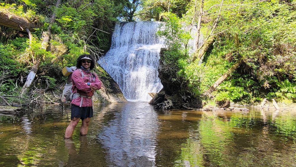 a hiker standing in water in front of a waterfall