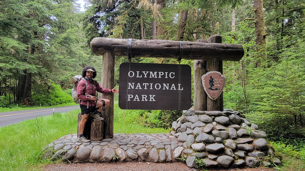 a hiker standing next to the Olympic National Park sign