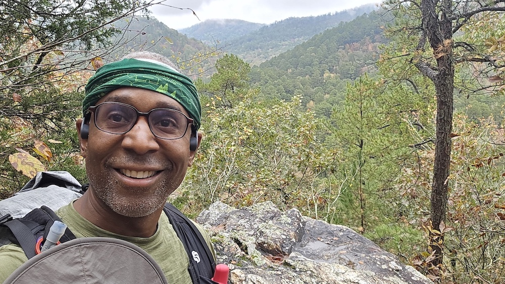 a hiker smiling with mountains and trees in the background