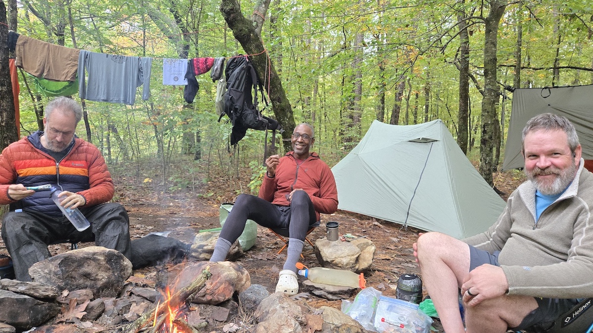 three hikers sitting around a fire at camp