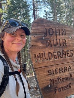 a hiker smiling next to the John Muir Wilderness sign
