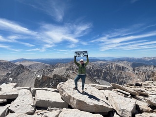 a hiker holding a sign over their head on top of Mt Whitney