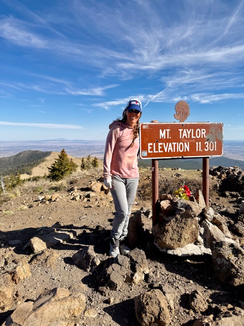 a hiker standing next to the Mt Taylor elevation sign