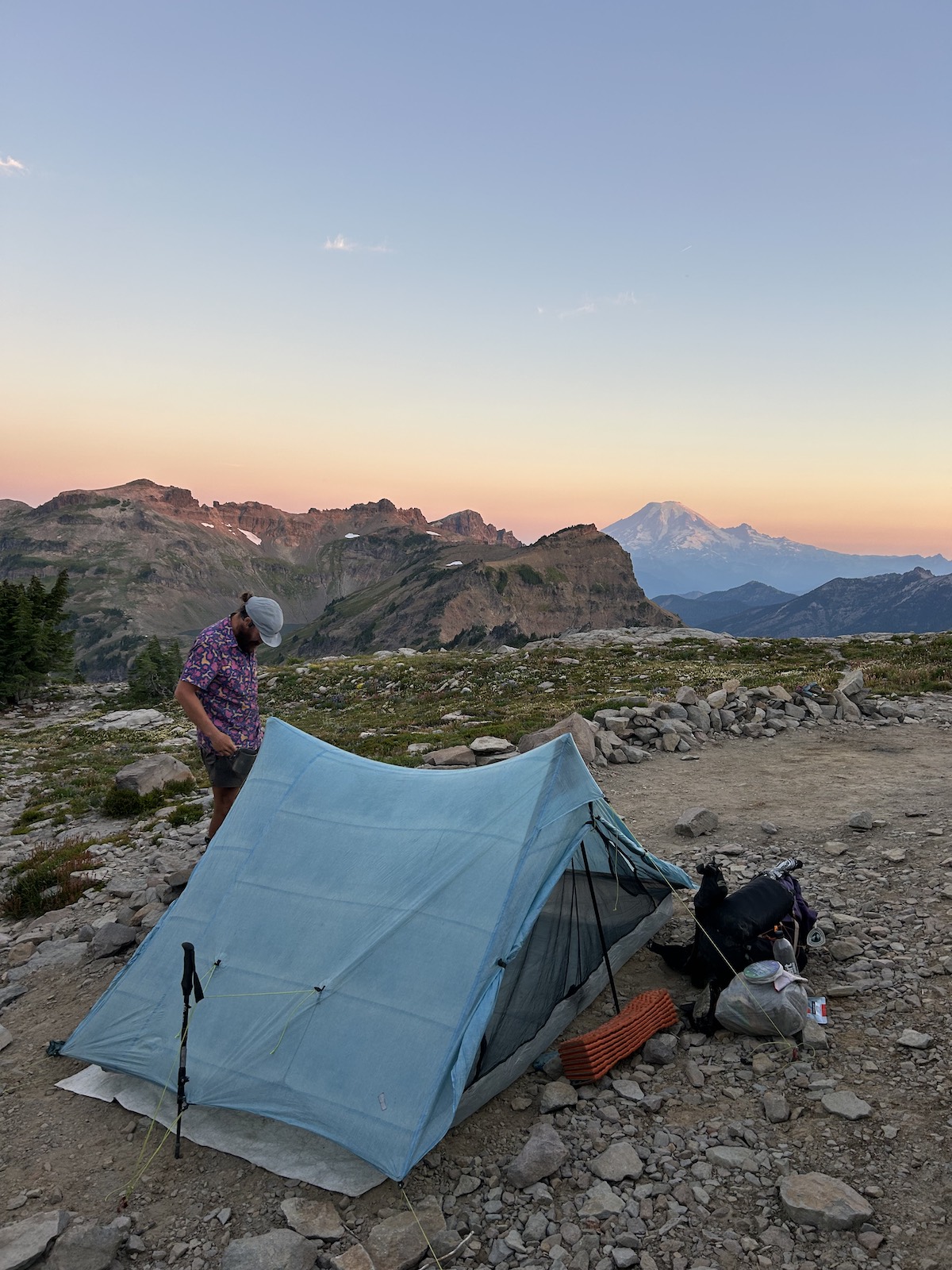 a hiker standing next to a tent with a sunset in the background