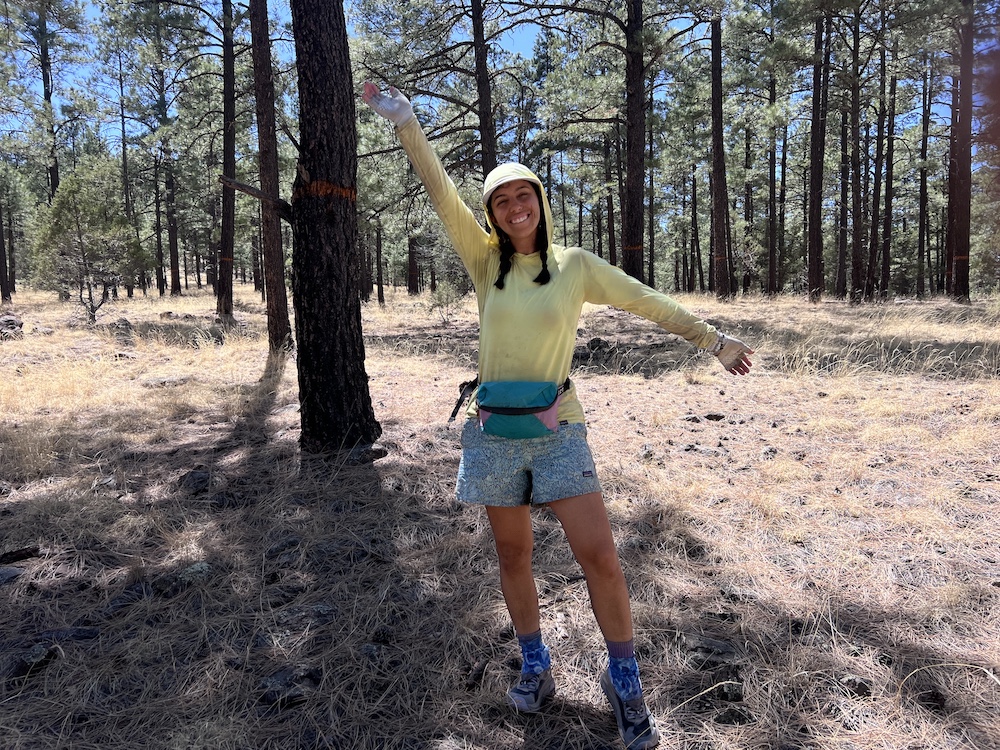 a hiker smiling with her arms out in the woods