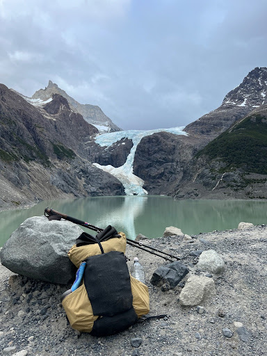 a backpack and trekking poles leaned up against a rock with a lake and mountains in the background