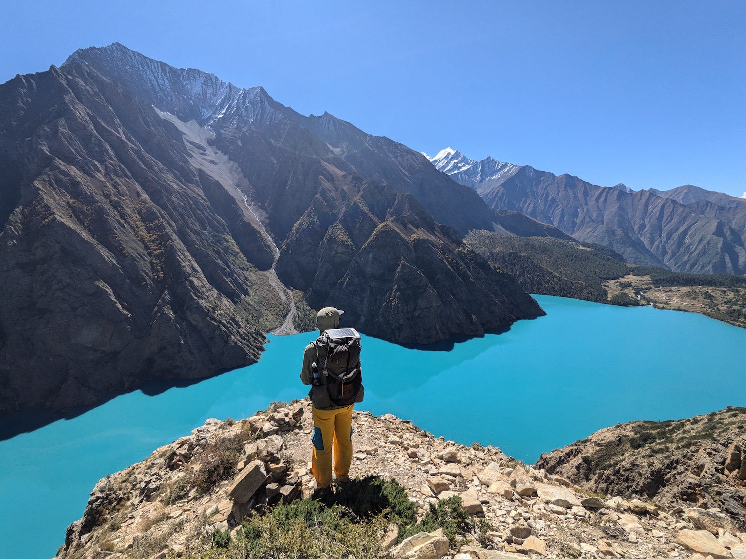 great-himalaya-trail-lake a hiker standing on a cliff with a lake and mountains in the background