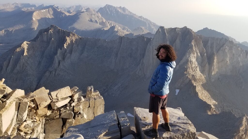a hiker standing on a mountain with other mountains in the background