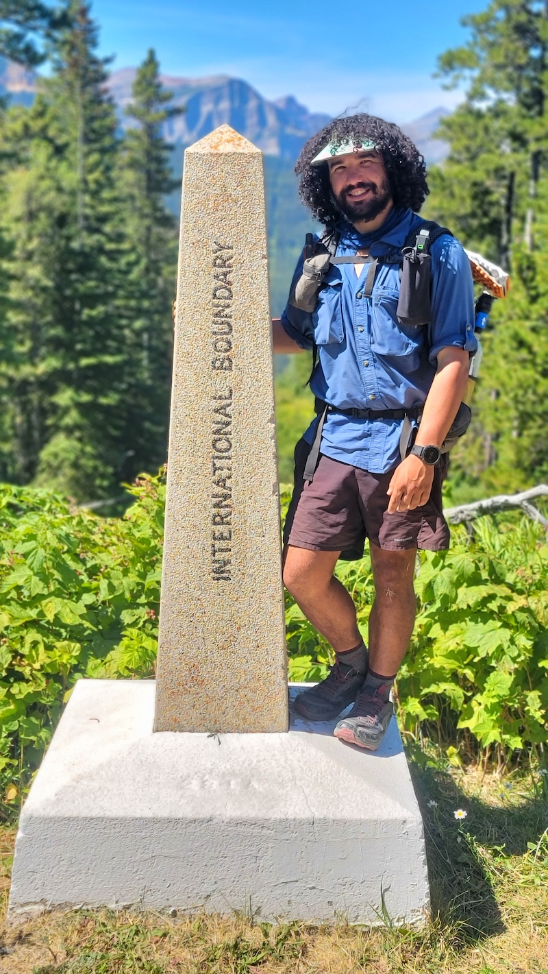 a hiker standing next to the cdt northern terminus