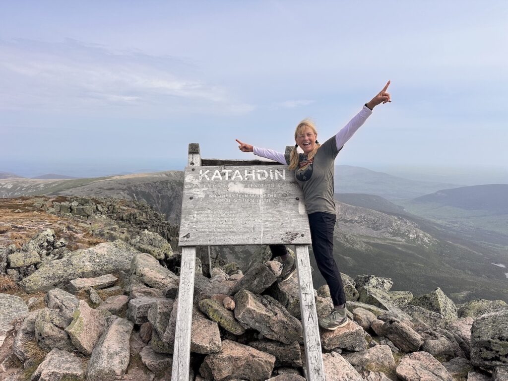 IMG_4533 a hiker smiling with her arms up next to the Katahdin trail sign