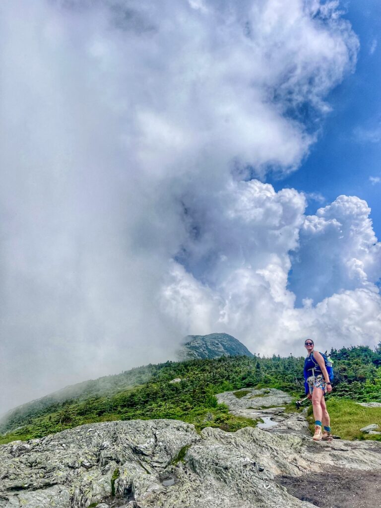 hiker_in_clouds a hiker standing on a hill with thick clouds in the background