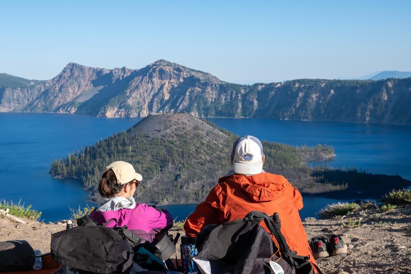 two hikers sitting looking out at a lake with a mountain surrounding it